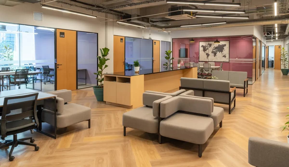 Área lounge con sillones grises y oficinas privadas en Flexo Del Valle