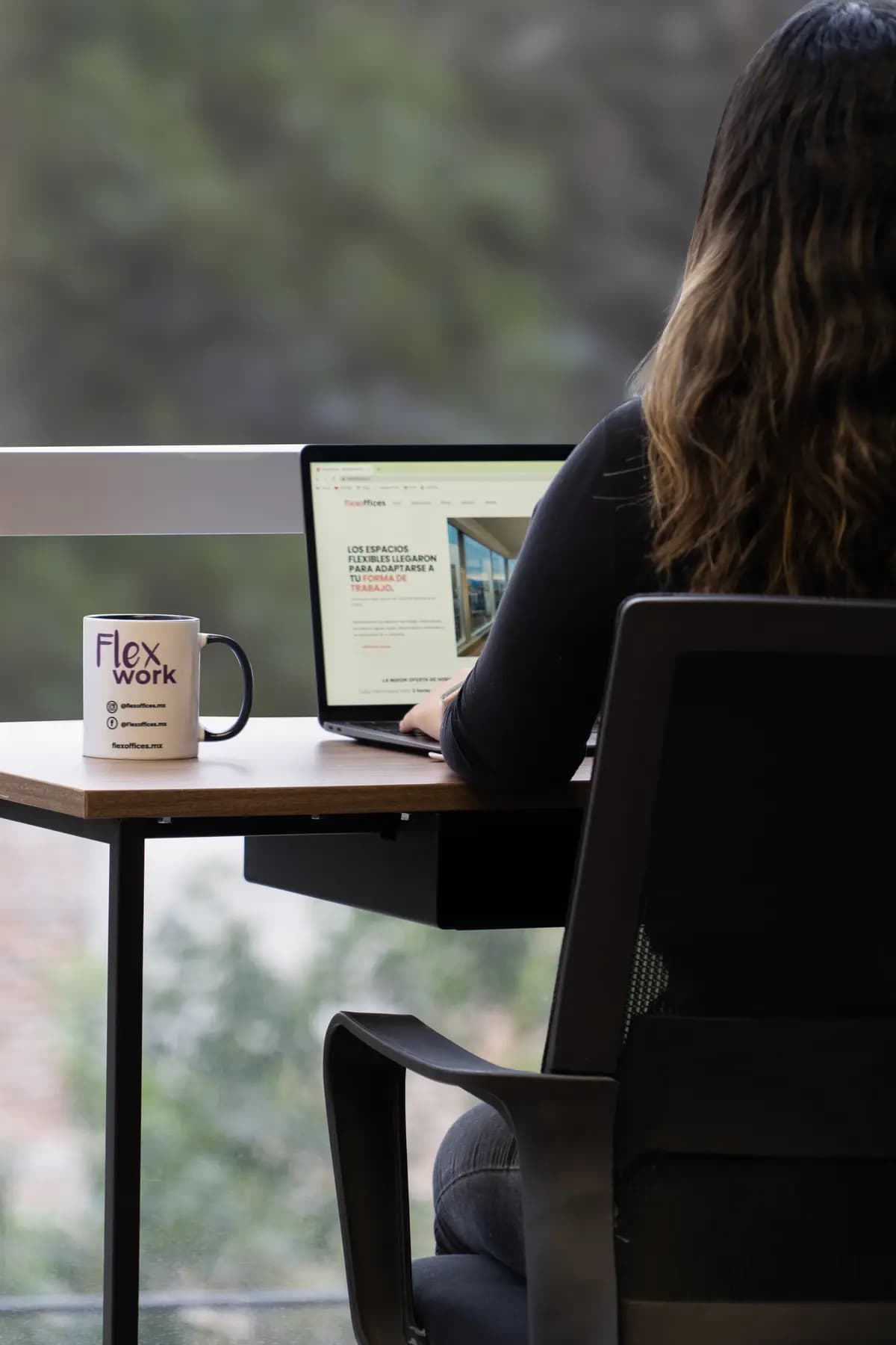 Persona trabajando junto a la ventana con una taza de Flexoffices